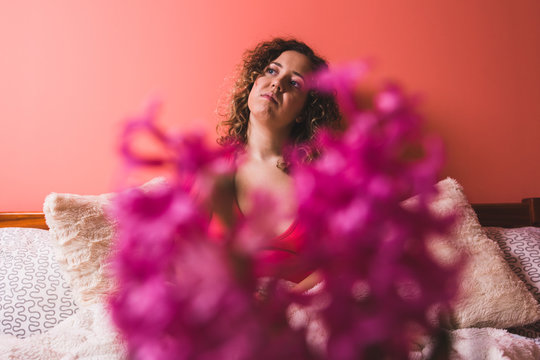 Beautiful curly woman thinking behind flowers. Selective focus. Hello Spring concept.
