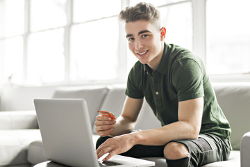 Handsome man using a laptop sitting on couch at home
