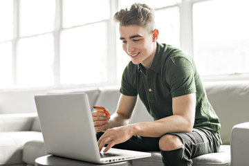 Handsome man using a laptop sitting on couch at home