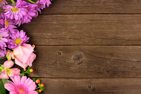 Side border of pink and purple flowers with rose, daisies and lilies against a rustic wood background. Copy space.