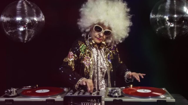 amazing DJ grandma scratching vinyl, older lady djing and partying in a disco setting. these retired rockers will get the party going.