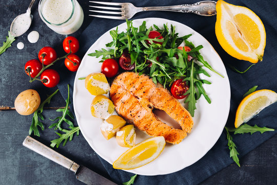 Grilled salmon with arugula and cherry tomato salad and potatoes on blue background