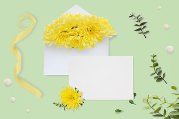 Letter, envelope and a present on pastel green background. Wedding invitation cards or love letter with chrysanthemums. Valentine's day or other holiday concept, top view, flat lay, overhead view.