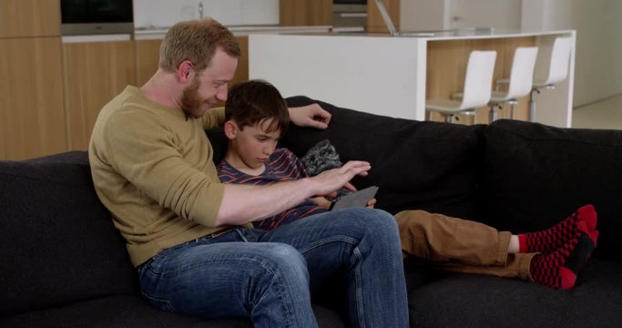 Attractive young father and son, websurfing on internet using tablet in contemporary home, in slow motion