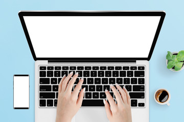Female hands typing on laptop keyboard with isolated screen on blue table surrounded with coffee, plant and phone. Responsive mockup of laptop and smartphone