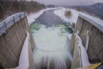 Above view of water reservoir with small dam. Small pile of snow and ice below the concrete dam....