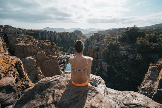 Rear view of woman in bikini while sitting on mountain against cloudy sky