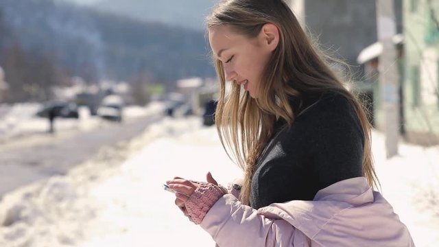 Woman using smart phone at winter city street in slow motion