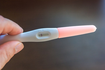 Hand holds negative pregnancy test over the brown background.
