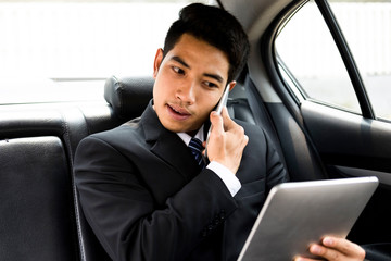 Busy businessman using mobile phone and tablet in car.