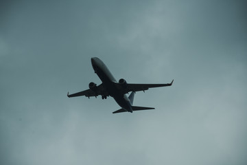 Silhouette of plane in grey sky. Passenger plane flies high in sky, flight. International flights, delivery, transportation. Flight and weather conditions concept.