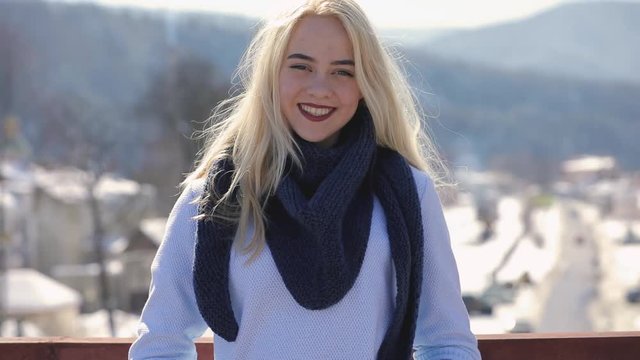 Young woman in sweater and scarf posing on a bridge at winter day