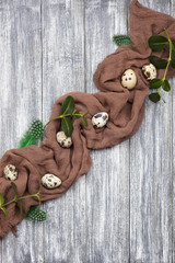 Easter decoration quail eggs with brown fabric on gray wooden background.