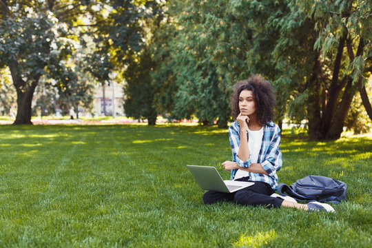 Serious young black woman using laptop in park