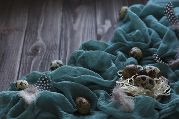 Easter decoration feathers quail eggs, green fabric on wooden brown background.