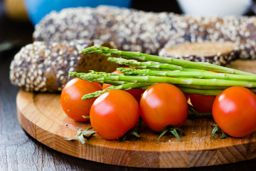 Fresh and ripe asparagus and cherry tomatoes with bread on wooden board.