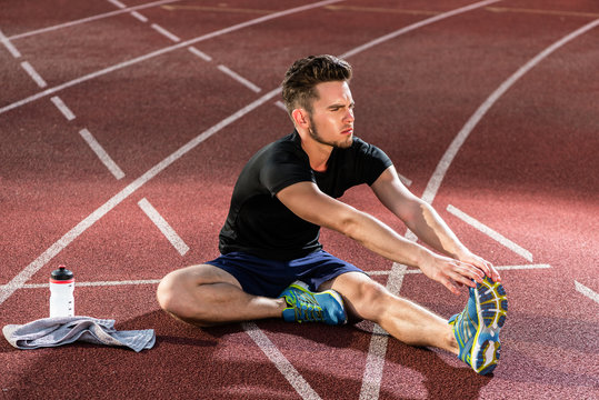 Young athlete stretching on racing track before running