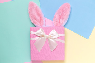 Bunny ears and present on plain multicolored background.