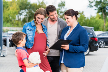 Car dealer advising family on buying auto showing price list