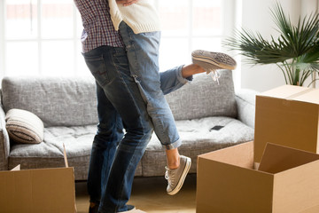 Happy couple on moving day concept, man lifting woman standing among cardboard boxes starting...