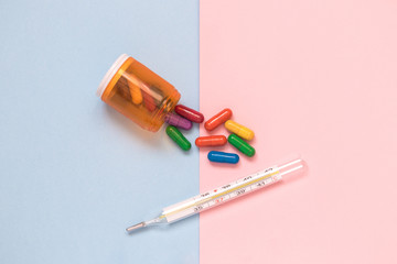 Multicolored medicines and thermometer isolated on pastel background minimalistic flat lay concept.
