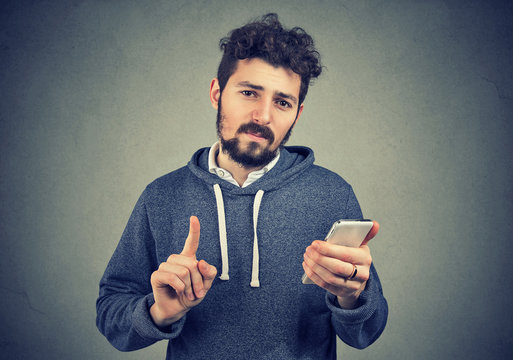 Man holding cell phone showing no, attention with finger hand gesture
