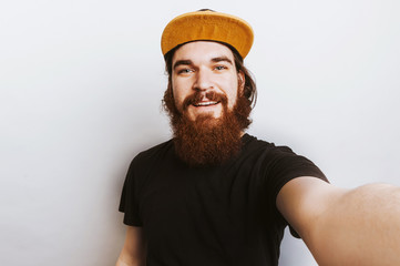 Happy bearded hipster man with cup taking selfie with camera over white background