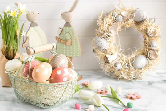 Cheerfull easter home decoration with painted egg basket, rabbits and spring wreath. Colorful easter image with harmony and freshness.