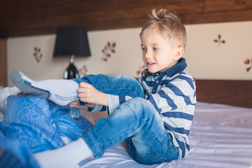 Five years old boy dresses his socks in the morning on the bed