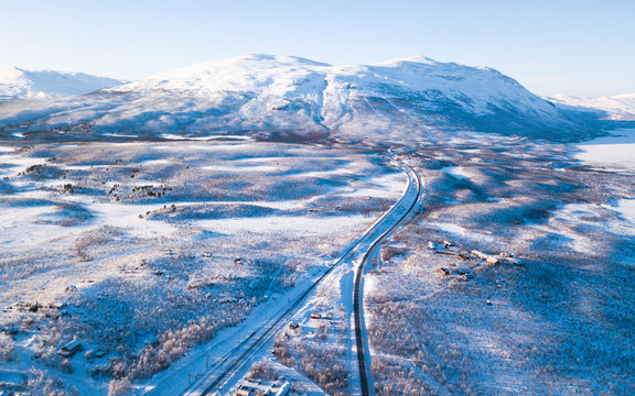 Aerial sunny winter view of Abisko National Park, Kiruna Municipality, Lapland, Norrbotten County, Sweden, shot from drone, with road and mountains
