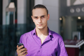 A handsome, young guy in a purple shirt is talking on the phone. Model of a man in a mall with a mobile phone in his hand