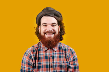 Happy smiling bearded hipster with hat looking confident at the camera over yellow background.