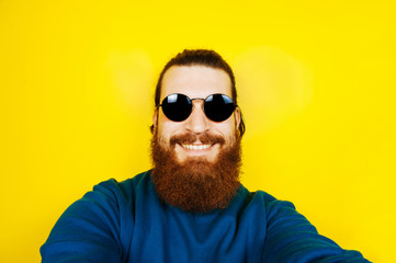 Fototapeta premium Portrait of young hipster man with beard in sunglasses taking a selfie. Smiling, happy man with beard.