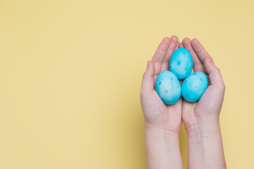 Creative concept of Easter. Hand save egg. Concept of good. Trendy blue polka dot eggs on pastel yellow background..