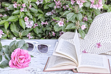 Pink rose, book, hat on the table in the garden