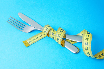 Paleo diet for weight loss. The fork and knife are wrapped in  yellow measuring tape on  blue...