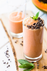 Vegan Papaya Smoothie Banana Milkshake Cacao Nibs and Mint on top on White Wooden Background