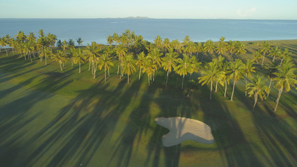 AERIAL: Flying over tranquil golf course illuminated by gentle evening sun rays.