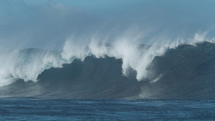 Massive emerald ocean swell breaks and sends countless water droplets flying.
