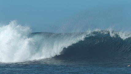 Big blue barrel wave crashes forcefully and splashes fresh sea water everywhere.