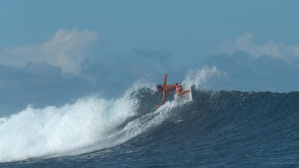 Athletic man on summer holiday does a sharp turn with his surfboard on big wave.