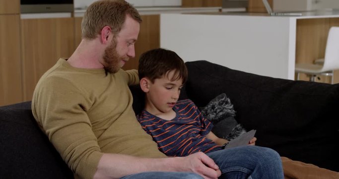 Attractive young father and son, websurfing on internet using tablet in contemporary home,