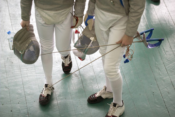 Legs of two young fencers holding swords and protective mask on the fencing competition