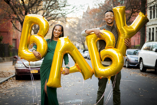 Portrait of happy expectant couple holding helium baby text balloons while standing on road in city