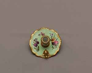 antique 18th century candle holder in porcelain decorated by hand with depictions of plants and animals on isolated gray background.