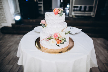Wedding cake. Beautiful white three-tiered wedding cake which standing on the table and decorated by flowers and greenery
