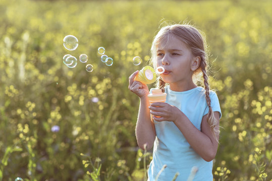 Portrait of calm female child inflating soap bubbles in the nature
