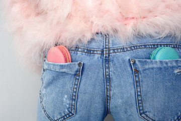 close-up of pink and minty macaroons that lie in the pockets of the girl's jeans in a pink fur coat turned back