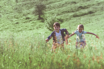 Fototapeta premium Joyful children are running on meadow. They are holding hands and laughing with excitement. Copy space