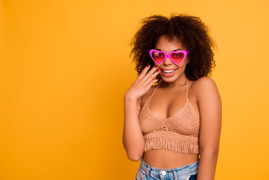 Portrait of lovely attractive careless afro shy woman with soft fluffy curly hair, wearing knitted beige summer top, she is touching and covering her cheeks with a hand, isolated on yellow background